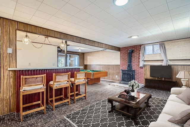 carpeted living room with a wealth of natural light, a wood stove, wood walls, and wainscoting