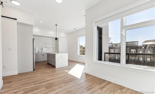 kitchen featuring pendant lighting, stainless steel fridge, backsplash, gray cabinets, and light wood-type flooring