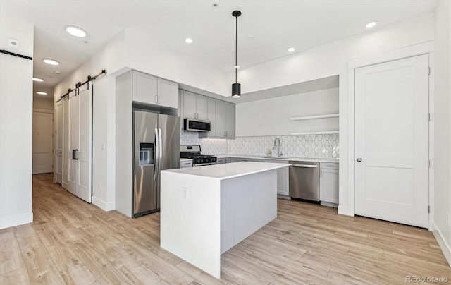 kitchen featuring a center island, tasteful backsplash, hanging light fixtures, a barn door, and stainless steel appliances