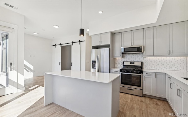 kitchen featuring gray cabinets, light hardwood / wood-style floors, a barn door, stainless steel appliances, and decorative light fixtures