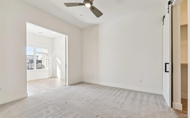 unfurnished room featuring light carpet, ceiling fan, and a barn door