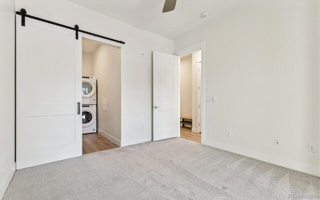 unfurnished bedroom with light carpet, a barn door, stacked washer / drying machine, and ceiling fan