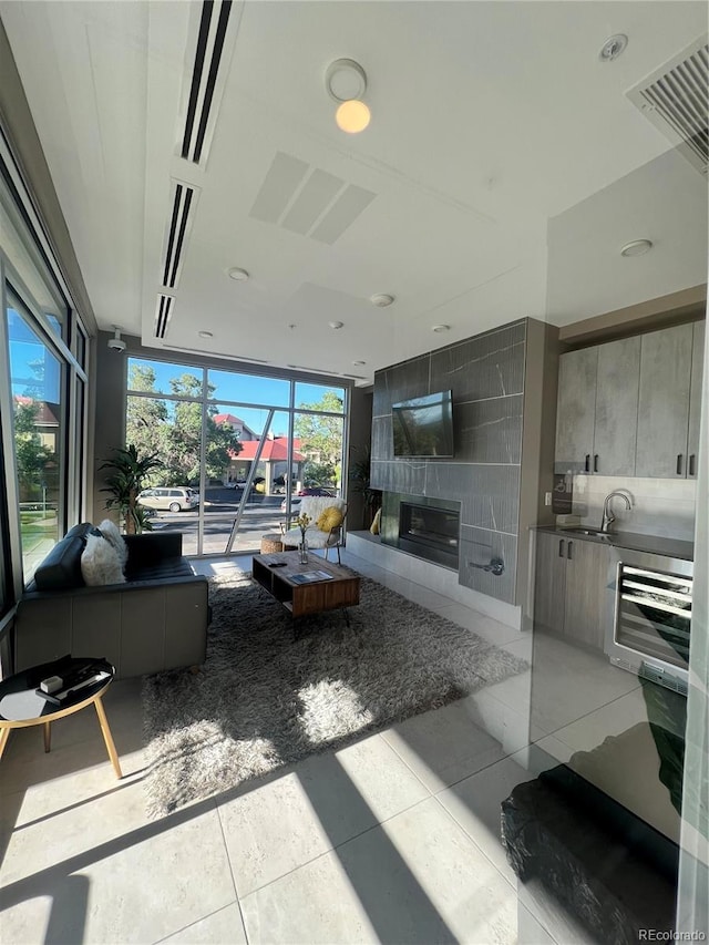 living room featuring a tiled fireplace, a wall of windows, light tile patterned flooring, and sink