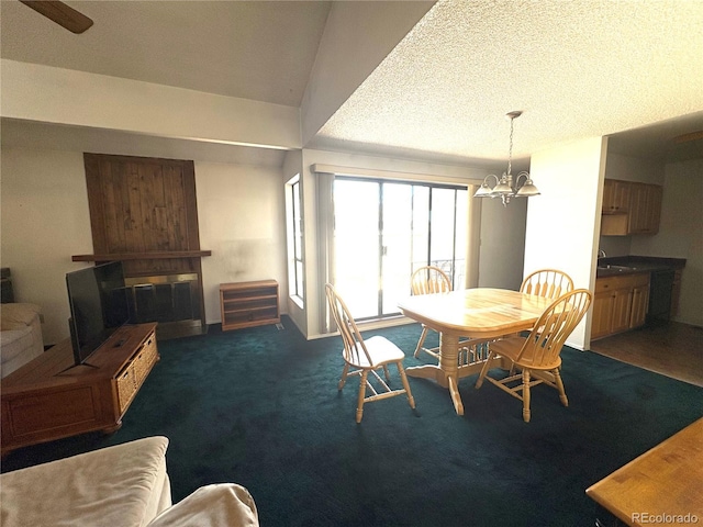 dining area with carpet floors, a textured ceiling, a notable chandelier, and a large fireplace