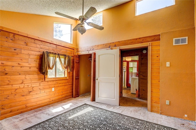 10893 Milliken Ave, Conifer, CO 80433 - unfurnished bedroom with light colored carpet, a towering ceiling, wooden walls, a textured ceiling, and a textured wall