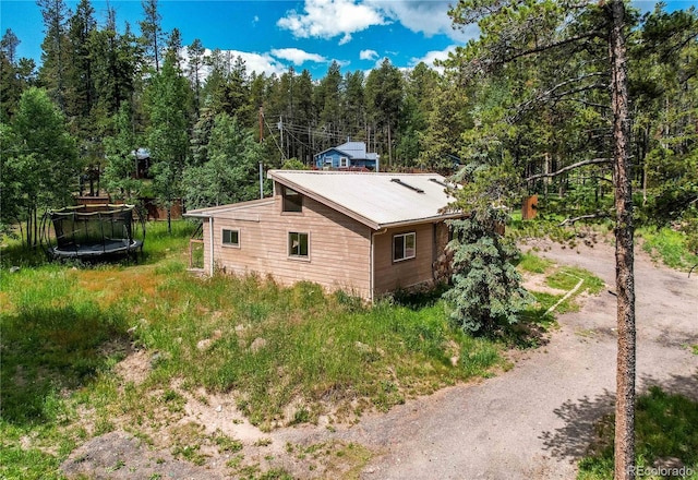10893 Milliken Ave, Conifer, CO 80433 - view of side of home featuring a trampoline, a wooded view, and a metal roof