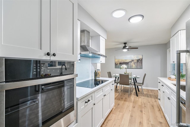 kitchen with white cabinetry, black electric stovetop, wall chimney exhaust hood, and ceiling fan