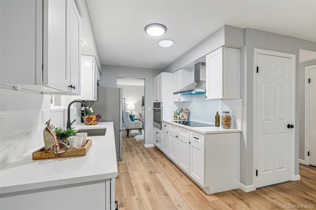 kitchen with white cabinets, light hardwood / wood-style flooring, wall chimney exhaust hood, stainless steel oven, and black electric stovetop