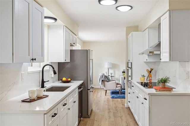 kitchen with appliances with stainless steel finishes, a sink, light countertops, light wood-style flooring, and white cabinetry