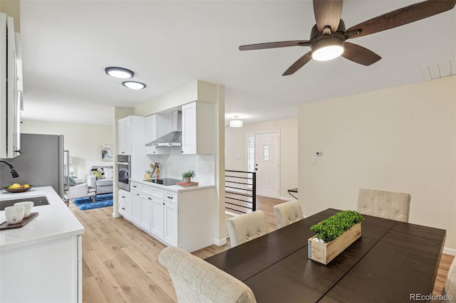 kitchen with appliances with stainless steel finishes, wall chimney exhaust hood, a sink, white cabinets, and light wood-style flooring
