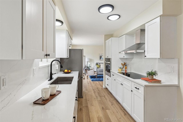 kitchen featuring wall chimney range hood, decorative backsplash, black electric cooktop, a sink, and oven