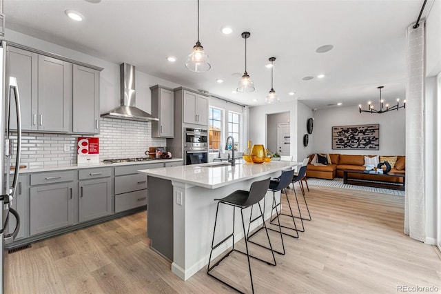 2110 Wagon Wheel Aly, Brighton, CO 80601 - kitchen with gray cabinets, wall chimney range hood, appliances with stainless steel finishes, light wood-style floors, and decorative backsplash