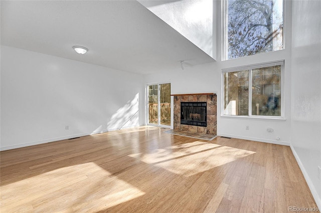 unfurnished living room with a tile fireplace, light hardwood / wood-style flooring, and a high ceiling