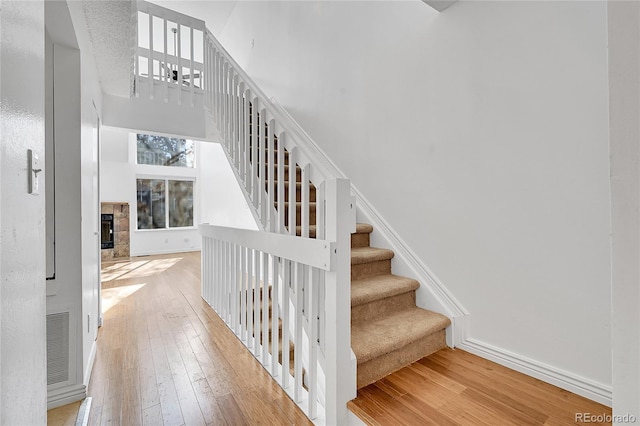 stairs with hardwood / wood-style flooring, a towering ceiling, and a fireplace