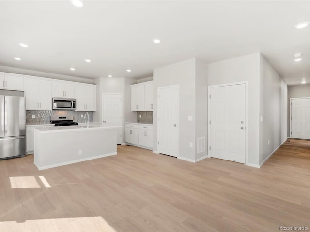 kitchen with light wood-style flooring, a sink, decorative backsplash, appliances with stainless steel finishes, and white cabinetry