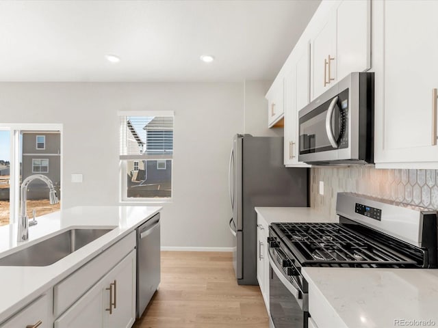 kitchen with tasteful backsplash, light wood-style flooring, white cabinets, stainless steel appliances, and a sink