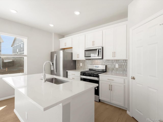 kitchen with backsplash, a center island with sink, appliances with stainless steel finishes, light wood-style floors, and a sink