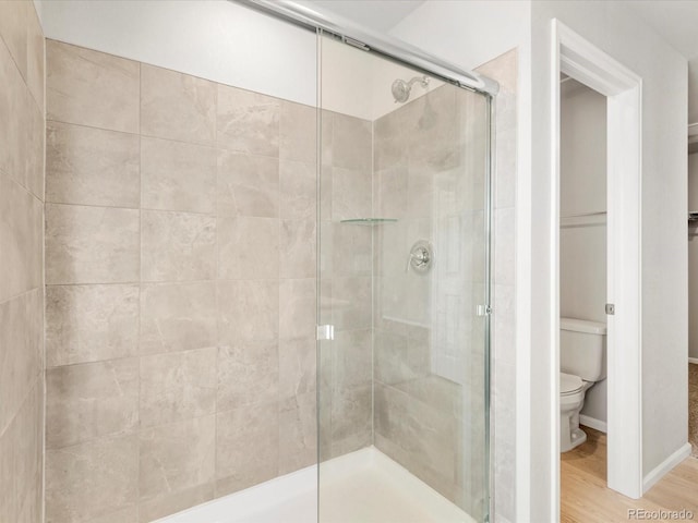 bathroom with a shower stall, toilet, baseboards, and wood finished floors