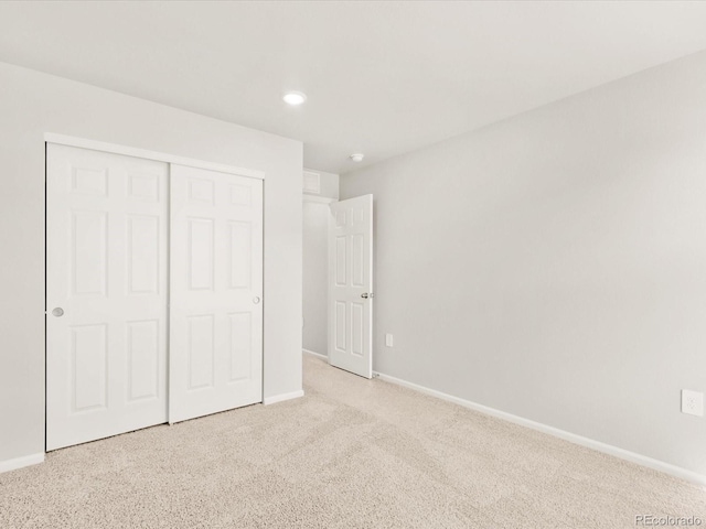 unfurnished bedroom with a closet, recessed lighting, light colored carpet, and baseboards