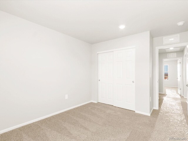 unfurnished bedroom featuring visible vents, baseboards, a closet, and light carpet