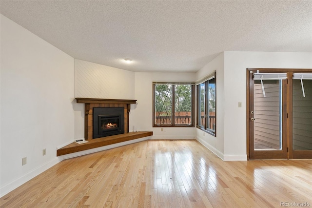 unfurnished living room featuring a tiled fireplace, a textured ceiling, and light hardwood / wood-style floors