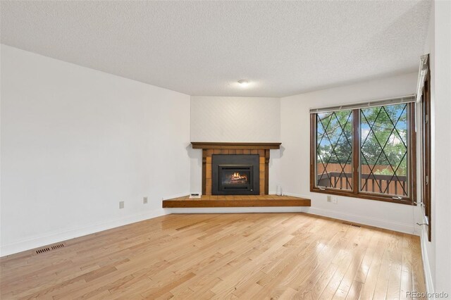 unfurnished living room with a fireplace, a textured ceiling, and light hardwood / wood-style floors