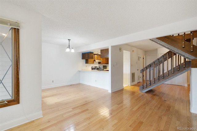 unfurnished living room featuring a textured ceiling, a notable chandelier, and light hardwood / wood-style floors