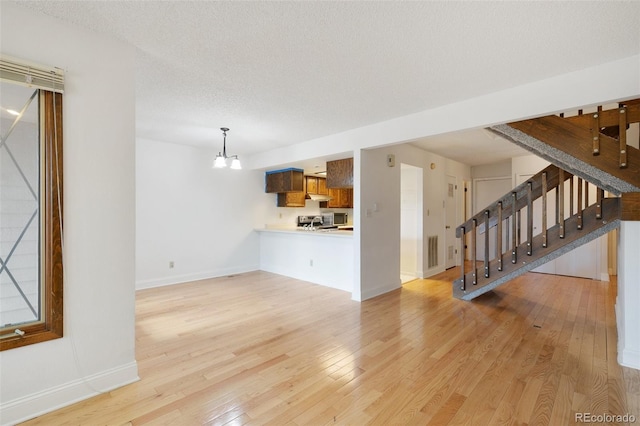 unfurnished living room featuring a notable chandelier, light hardwood / wood-style flooring, and a textured ceiling