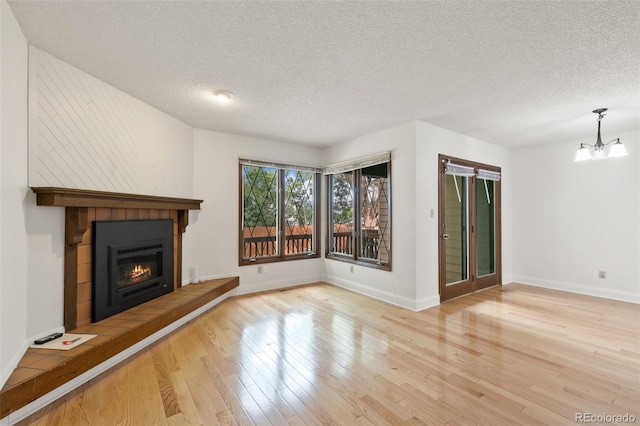 unfurnished living room with a notable chandelier, light wood-type flooring, a textured ceiling, and a tile fireplace