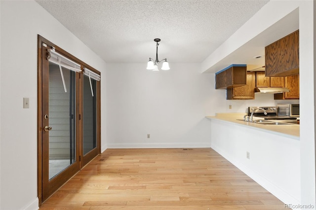 kitchen featuring a textured ceiling, hanging light fixtures, a notable chandelier, light wood-type flooring, and range