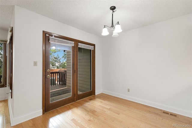 interior space featuring a healthy amount of sunlight, an inviting chandelier, a textured ceiling, and light hardwood / wood-style floors