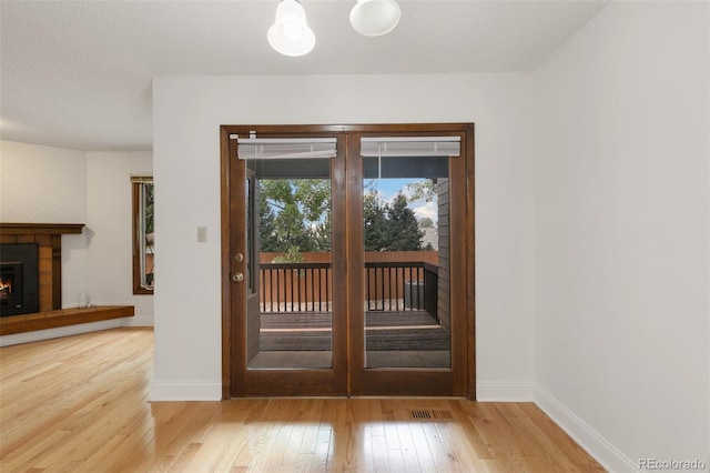 doorway to outside with a tile fireplace and light wood-type flooring