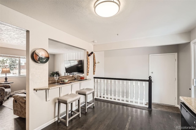 kitchen featuring a textured ceiling, a breakfast bar area, black dishwasher, open floor plan, and dark wood-style floors