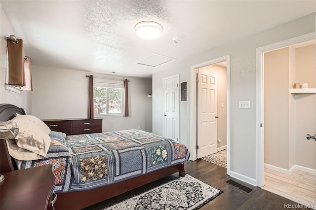 bedroom featuring attic access, baseboards, visible vents, dark wood-type flooring, and a textured ceiling