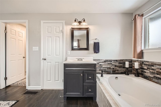 bathroom featuring a garden tub, visible vents, vanity, wood finished floors, and baseboards