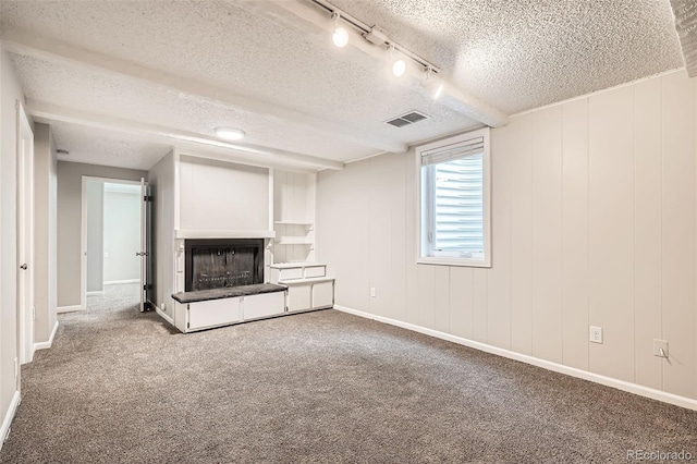 unfurnished living room with a fireplace with raised hearth, a textured ceiling, carpet floors, visible vents, and baseboards