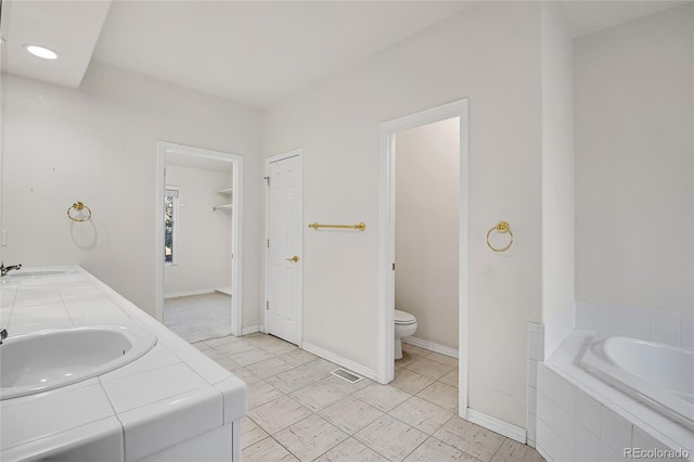 bathroom with tiled bath, a sink, toilet, and baseboards