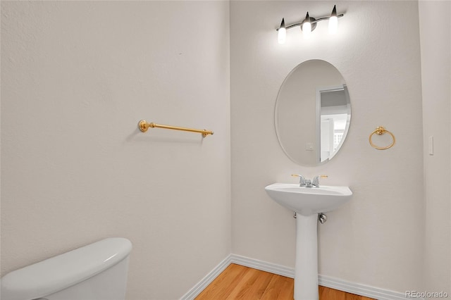 half bathroom featuring wood finished floors, toilet, and baseboards