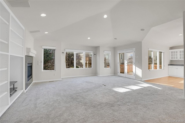 unfurnished living room featuring light colored carpet, a glass covered fireplace, a wealth of natural light, and recessed lighting