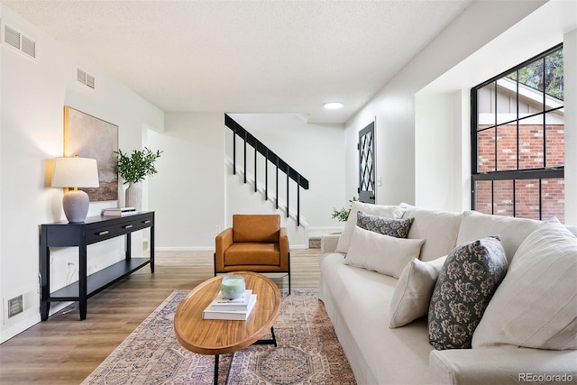 living area featuring a textured ceiling, visible vents, stairway, and wood finished floors