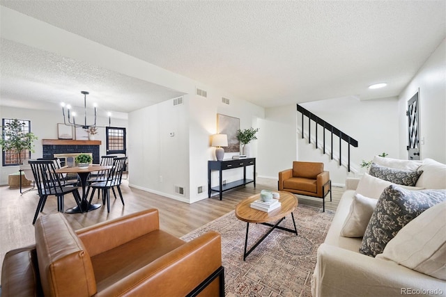 living room with a notable chandelier, stairway, light wood finished floors, and visible vents