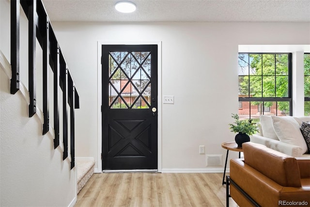entrance foyer with stairs, baseboards, a textured ceiling, light wood finished floors, and visible vents