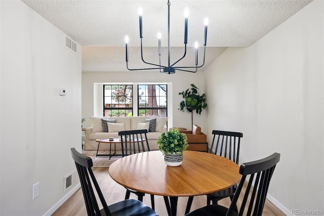 dining space featuring an inviting chandelier, a textured ceiling, light wood-style floors, and visible vents