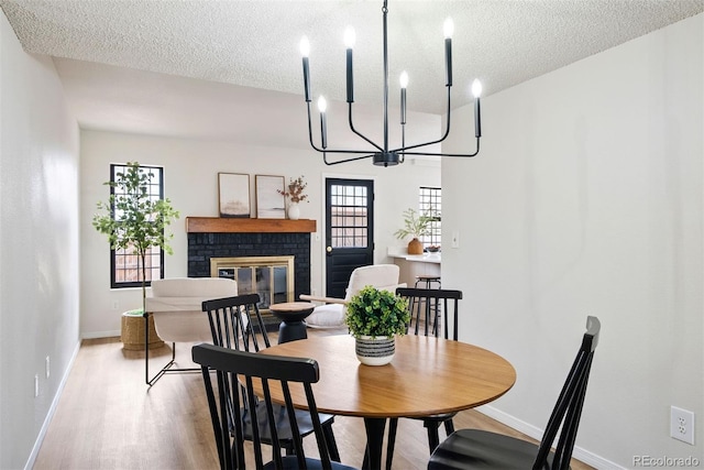 dining space with wood finished floors, a textured ceiling, a brick fireplace, baseboards, and an inviting chandelier