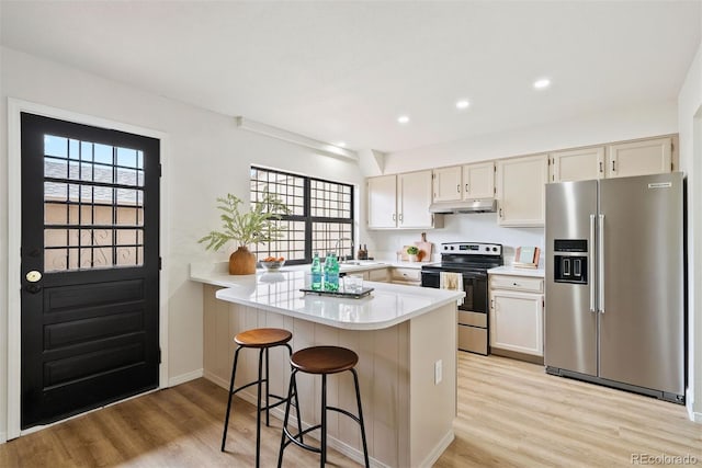 kitchen with light countertops, a peninsula, light wood-type flooring, under cabinet range hood, and stainless steel appliances