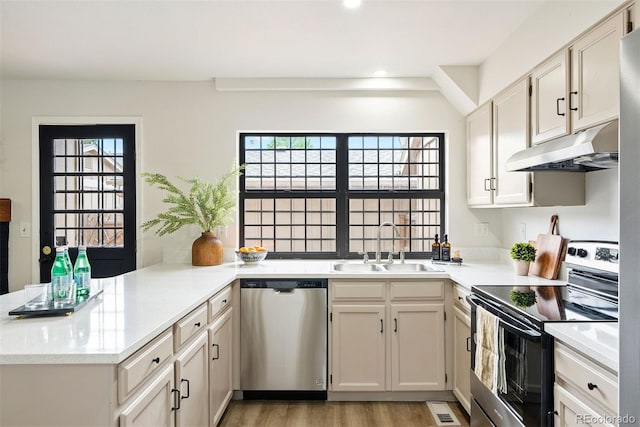 kitchen featuring a peninsula, stainless steel appliances, under cabinet range hood, a sink, and light wood-type flooring