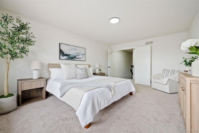 bedroom featuring a textured ceiling, light colored carpet, and visible vents