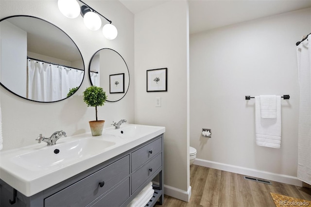 full bath featuring baseboards, a sink, visible vents, double vanity, and wood finished floors