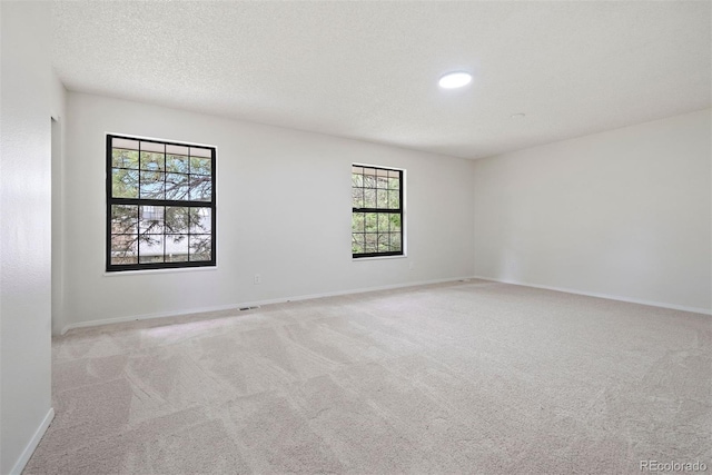 carpeted spare room featuring baseboards, a textured ceiling, and visible vents
