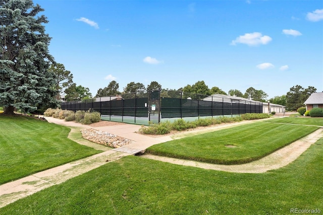 view of community with a yard, a tennis court, and fence